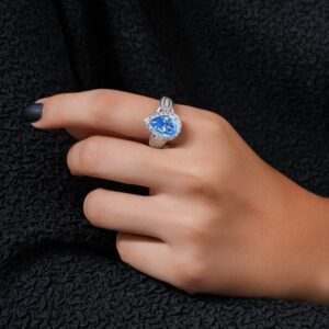 Close-up of an elegant blue gemstone ring worn on a hand with dark textile background.