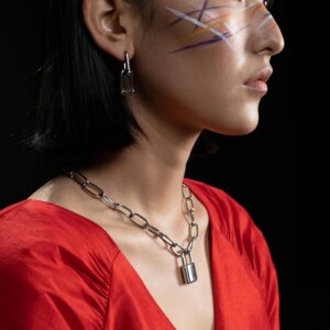 Artistic side profile portrait of a woman with face paint and bold jewelry on a black background.